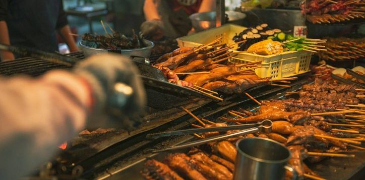 street-food-stall-with-many-skewers-grilling-over-open-heat-and-hands-preparing-food