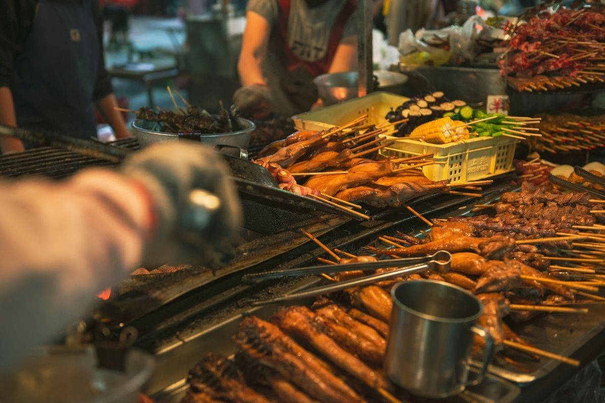 street food stall with many skewers grilling over open heat and hands preparing food