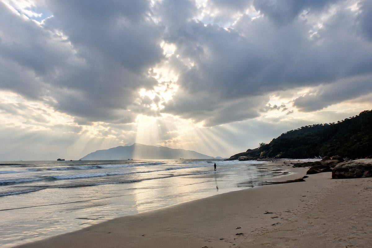 Sun rays breaking through clouds over Lang Van Beach with white sand and green mountains