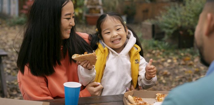 family-eating-pizza-outdoors-side-view