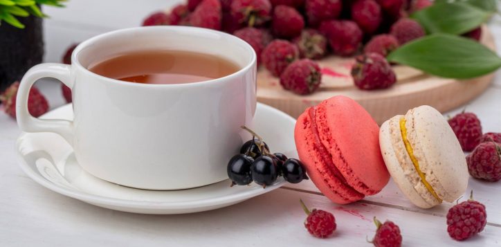 front-view-cup-tea-with-macaroon-raspberries-white-surface