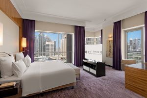 Premium Executive Room at Pullman Dubai Jumeirah Lakes Towers featuring a plush king-size bed, warm wood paneling, and a large window with city views.