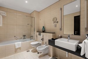 Modern, spacious marble bathroom with a bathtub, large mirror, and black vanity counter at Pullman Dubai Jumeirah Lakes Towers hotel room.
