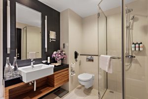 Modern hotel bathroom with a glass walk-in shower, wooden vanity with white vessel sink, and large mirror at Pullman Dubai Jumeirah Lakes Towers.