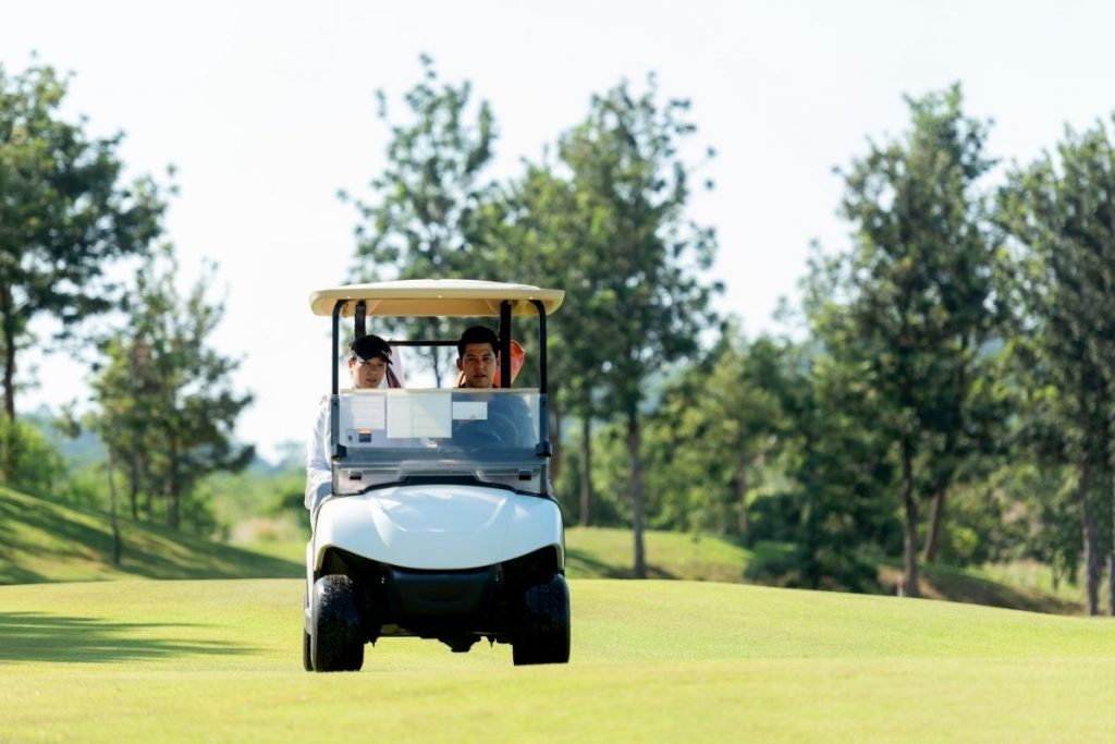 Couple riding a golf cart across a sunny green course with trees in the background