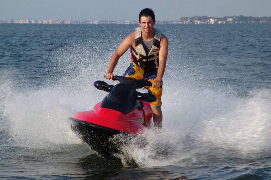 Person riding a red jet ski across the water with splashes all around