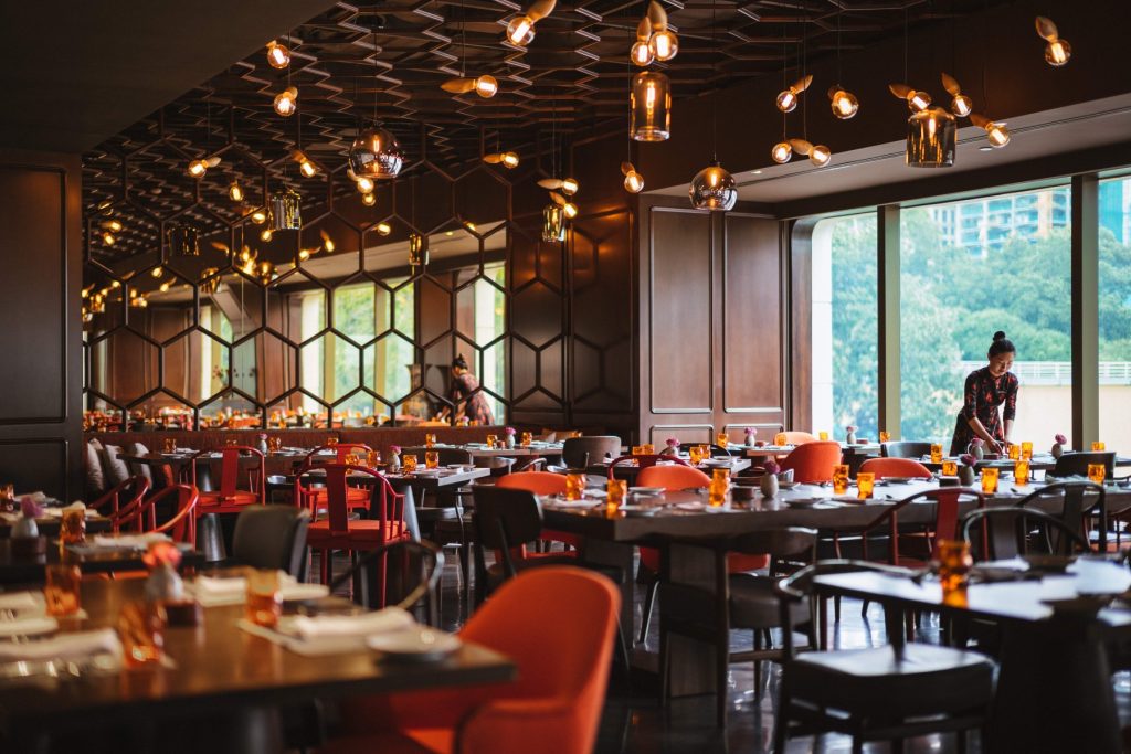 ALT TEXT: Saigon Kitchen at Hotel Des Arts Saigon: A chic dining space featuring vibrant orange and earthy tones, contemporary decor inspired by Asian street markets, and large windows offering natural light, creating a warm and inviting atmosphere.