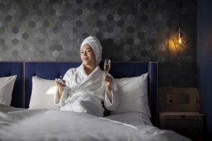 female with bathrobe on the bed drinking a glass of champaign and watching TV in privilege room