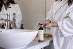 female with bathrobe pushing the bottle of body lotion in the bathroom