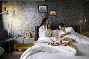 female and male eating and drinking with bathrobe on the bed in the deluxe room